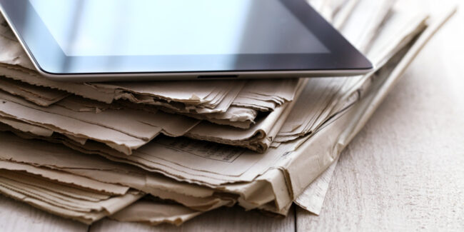 iPad appoggiato su una pila di giornali. Documenti appoggiati su un tavolo.