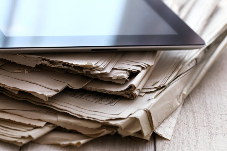 iPad appoggiato su una pila di giornali. Documenti appoggiati su un tavolo.
